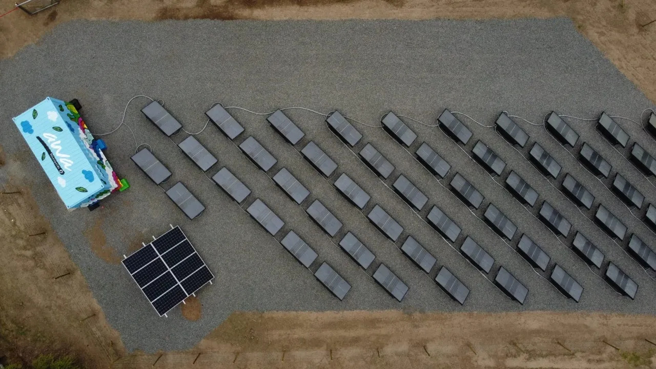 An aerial view of a solar farm showing rows of solar panels with cables connected to an energy storage system housed in a colorful container.