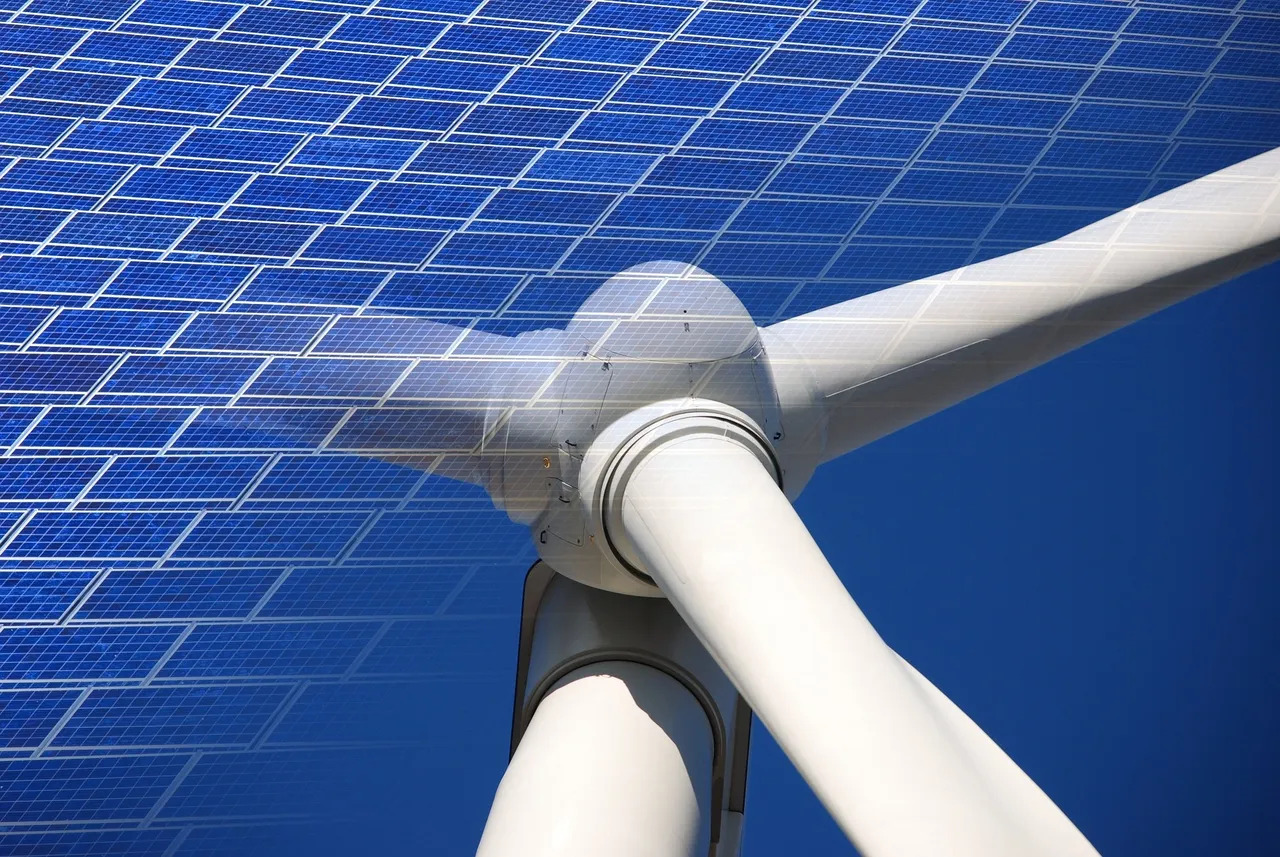 This image showcases a solar panel array against a clear blue sky, juxtaposed with a close-up of a white wind turbine's hub and blades.