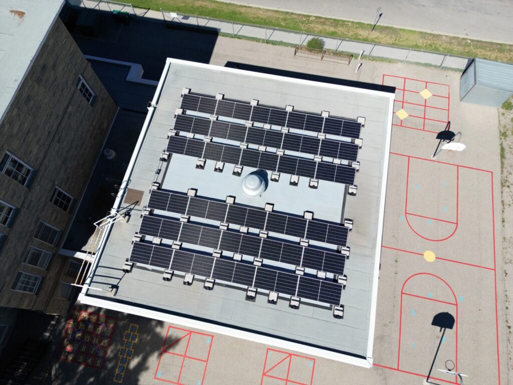 An aerial view of a building rooftop covered with solar panels alongside a playground with a basketball court and colorful ground markings.