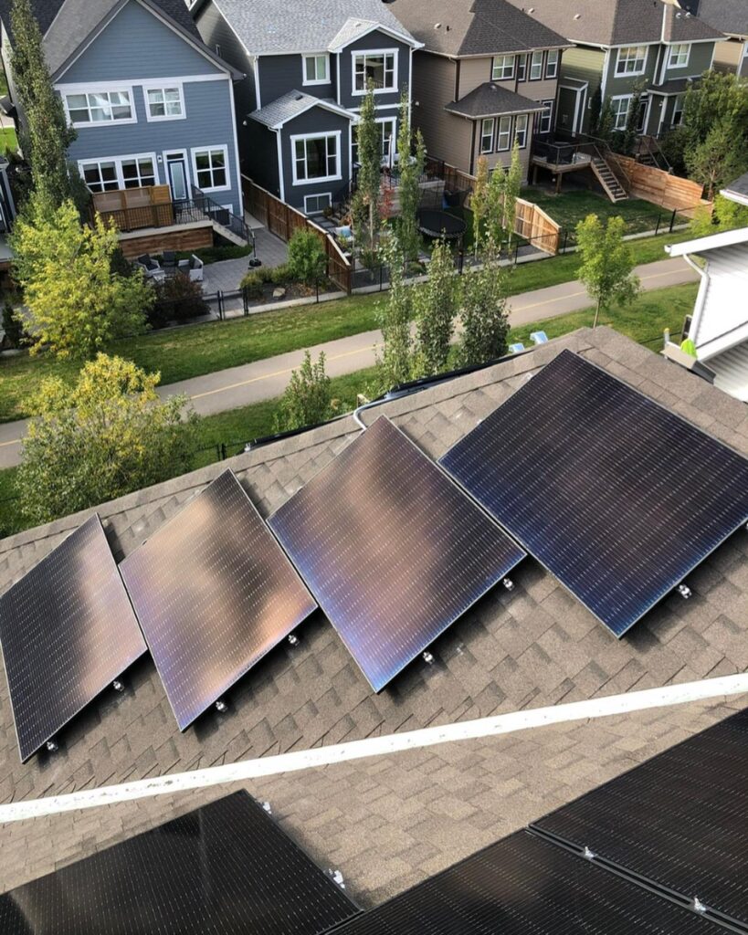 This image shows a rooftop with solar panels overlooking a suburban neighborhood with well-maintained houses and green trees lining the street.