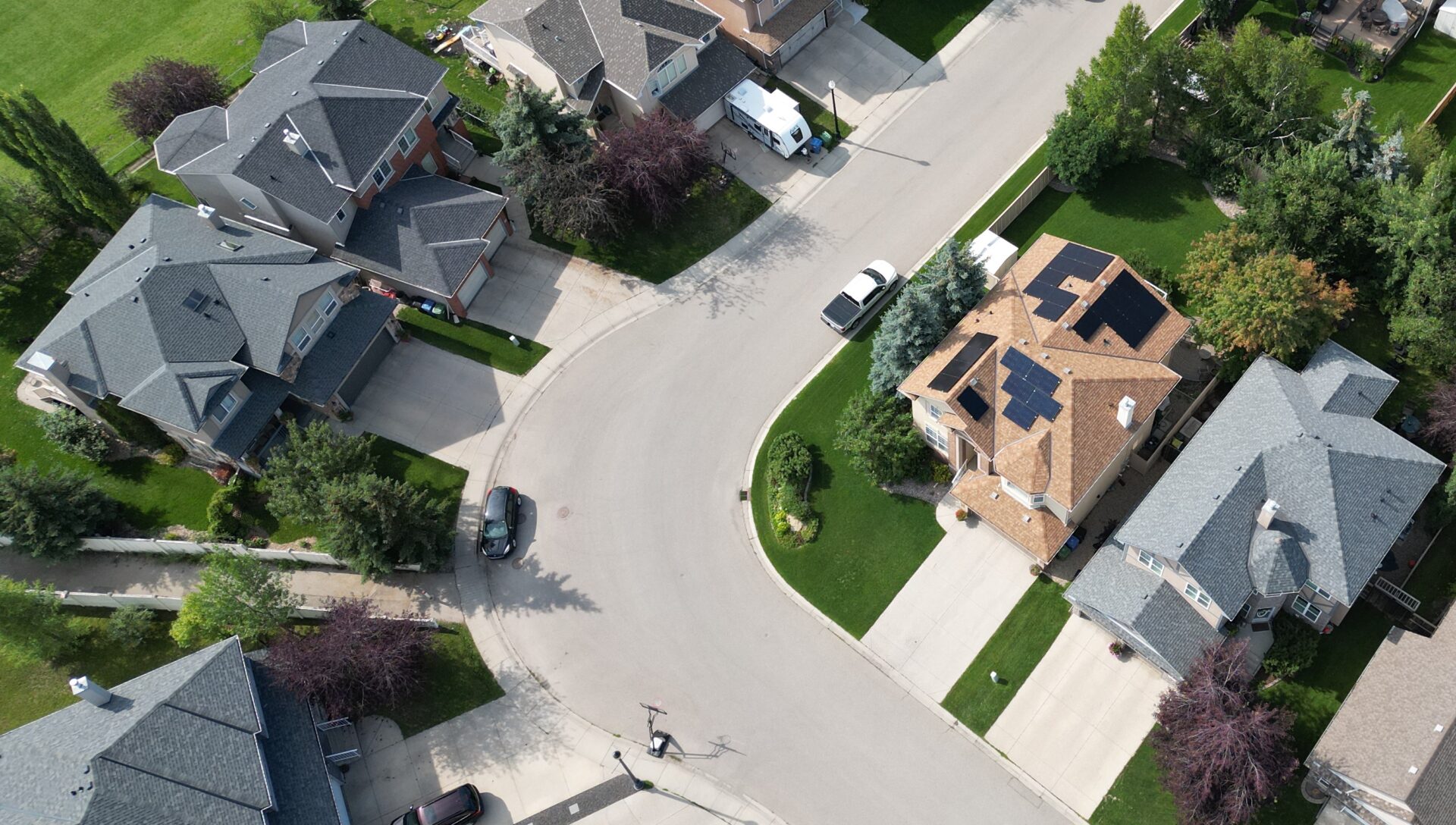 Aerial view of a suburban cul-de-sac showing detached houses with pitched roofs, well-manicured lawns, driveways with parked cars, and leafy trees.