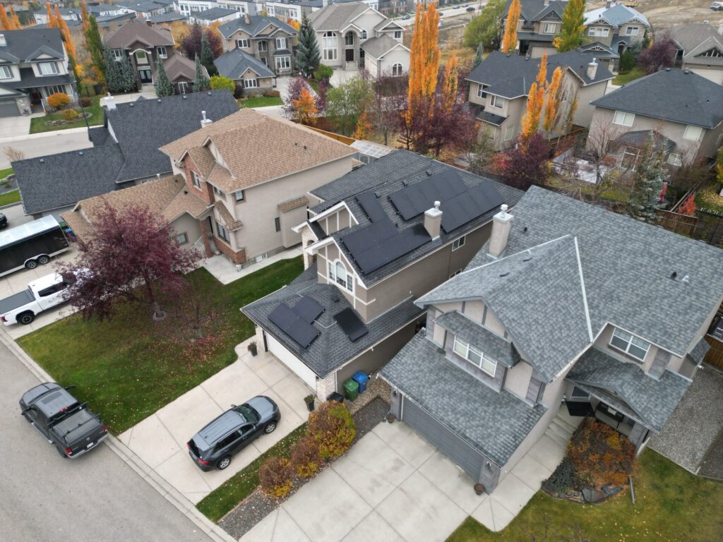 Aerial view of a residential neighborhood with detached houses, colorful fall trees, and parked cars. The overcast sky suggests a cool climate.