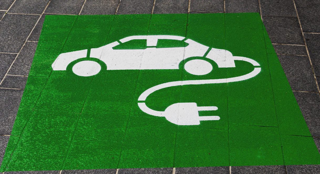 A green parking space with a white icon of an electric vehicle and a charging plug, symbolizing a dedicated electric car charging spot.