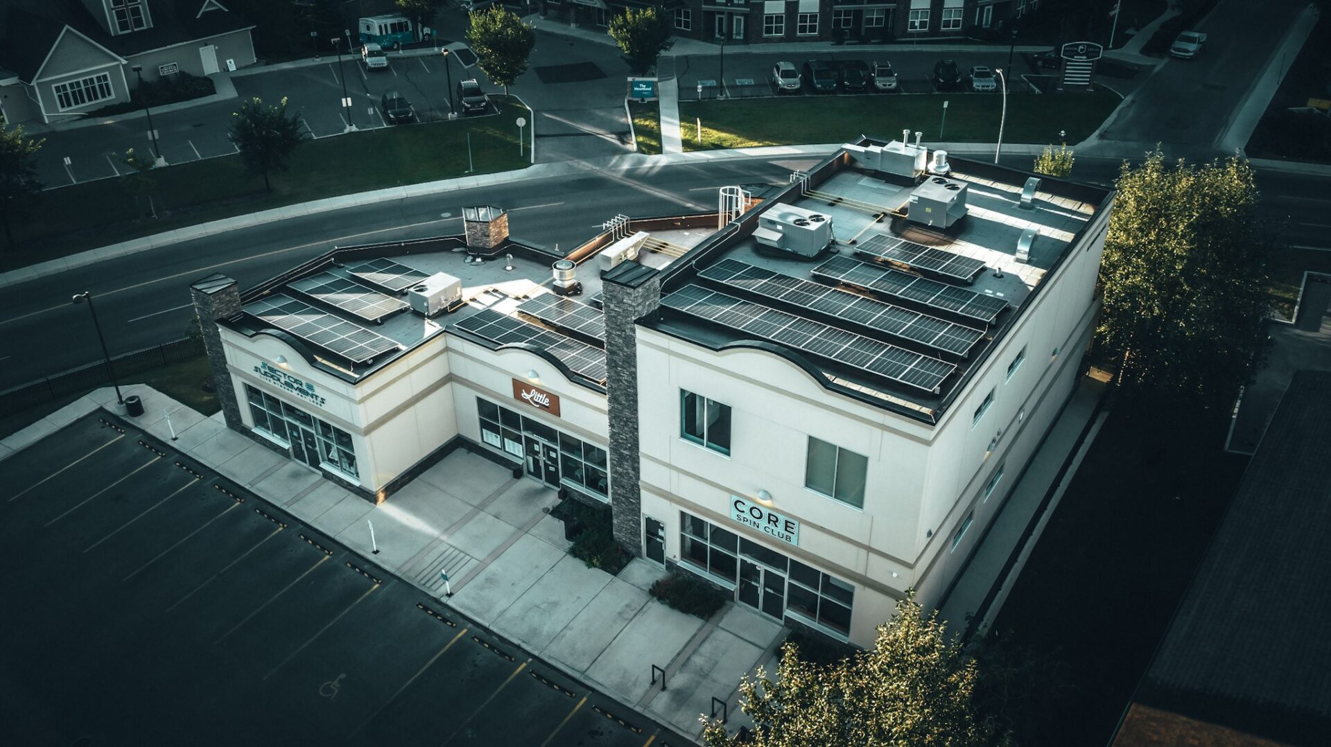 Aerial view of a two-story commercial building with solar panels on the roof, situated at a street corner, with a clear sky above.