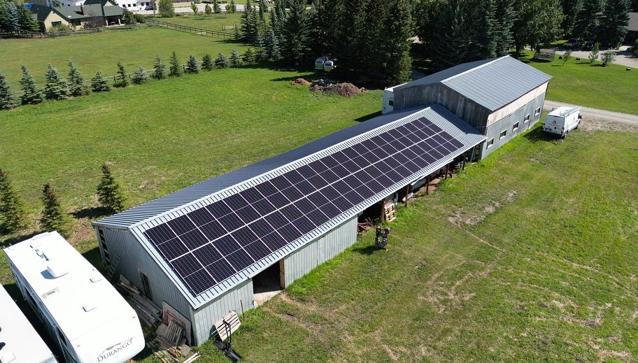 Aerial view of a rural landscape with large buildings equipped with solar panels on the roofs, recreational vehicles parked nearby, surrounded by greenery.