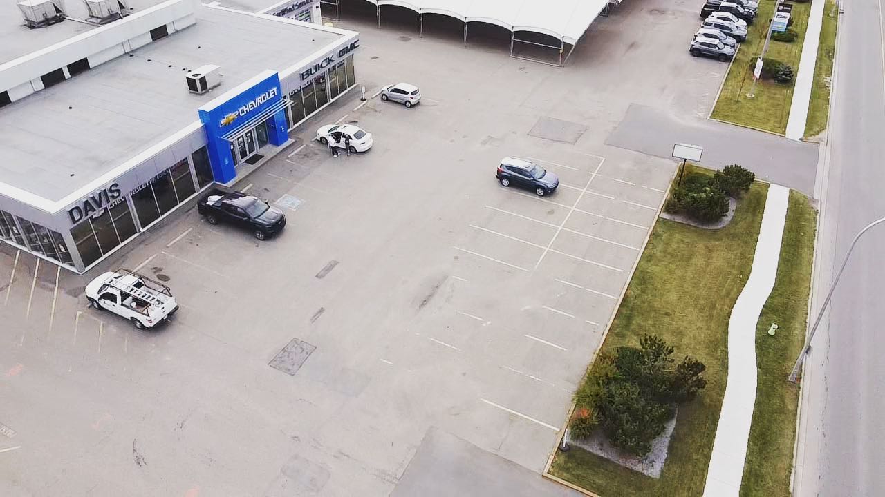 Aerial view of a car dealership with Chevrolet and Buick logos, featuring a parking lot with cars, landscaped areas, and an adjacent road.