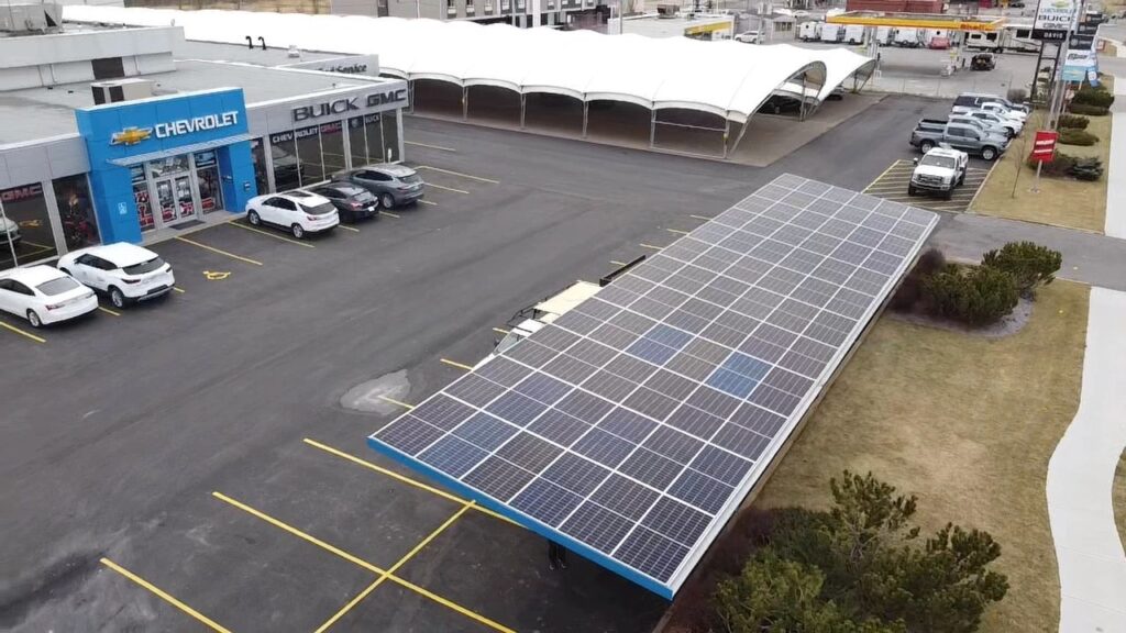 An aerial view of a car dealership displaying Chevrolet and Buick GMC brands with a large solar panel array in the parking area.