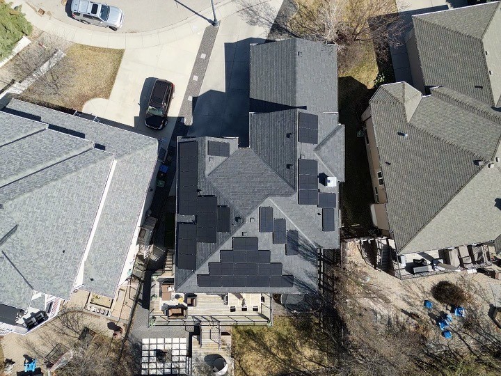 Aerial view of a residential area, showcasing rooftops, solar panels, a backyard with patio furniture, a vehicle, and bare trees indicating a non-summer season.