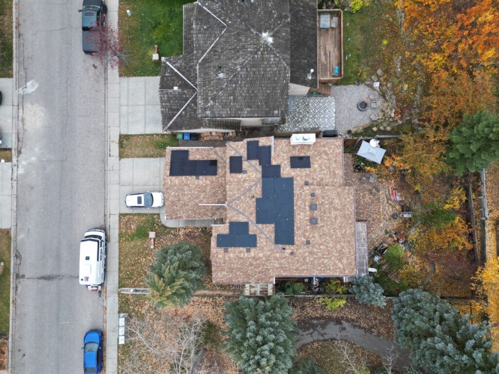 Aerial view of a residential area in autumn, showing houses with shingled roofs, vehicles, trees with fall foliage, and a neatly organized backyard.