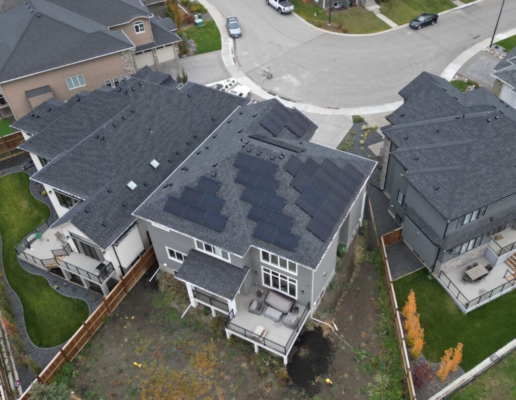 An aerial view of a suburban neighborhood with houses featuring solar panels on roofs, neat gardens, and an overcast sky above.