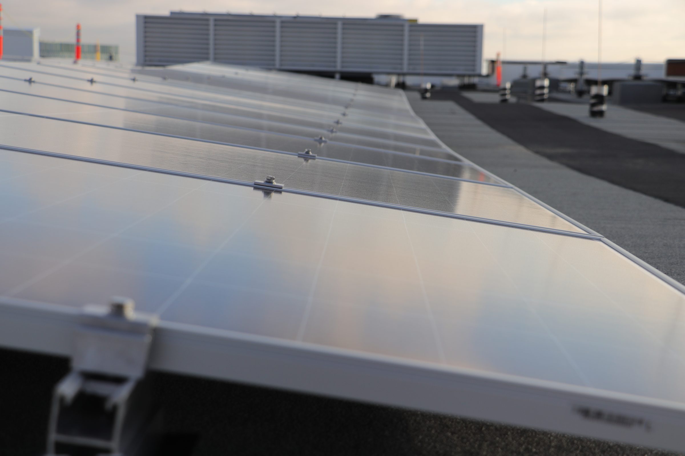 Commercial flat-roof solar panel installation on a non-ballasted racking system with a clear blue sky.